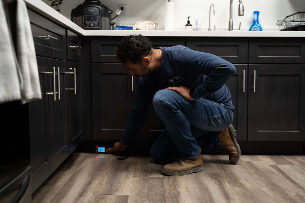 Preferred Choice technician checking a kitchen floor for hidden water with a moisture meter